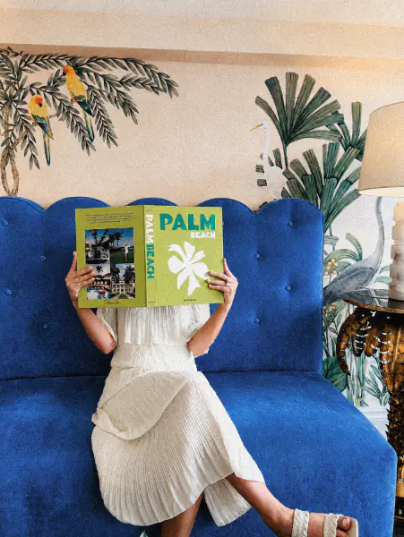 Woman reading a Palm Beach book on a blue velvet sofa