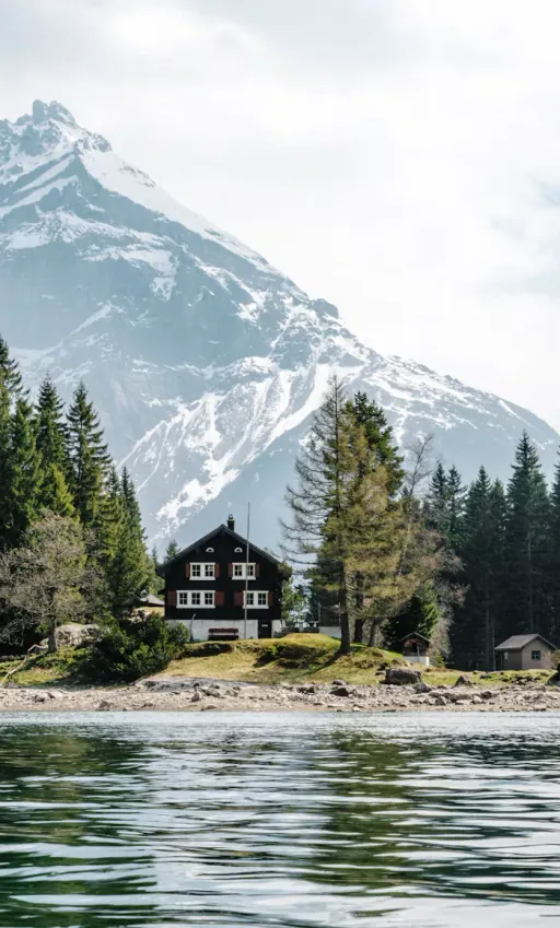 Swiss chalet on a lake shore below a snow-capped peak