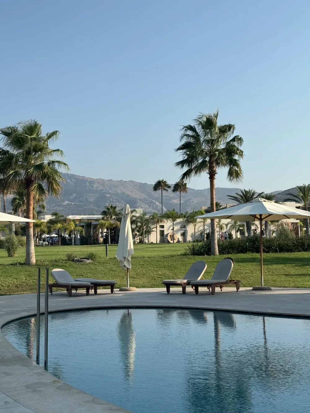 Hotel pool with sun loungers, palms and mountains beyond