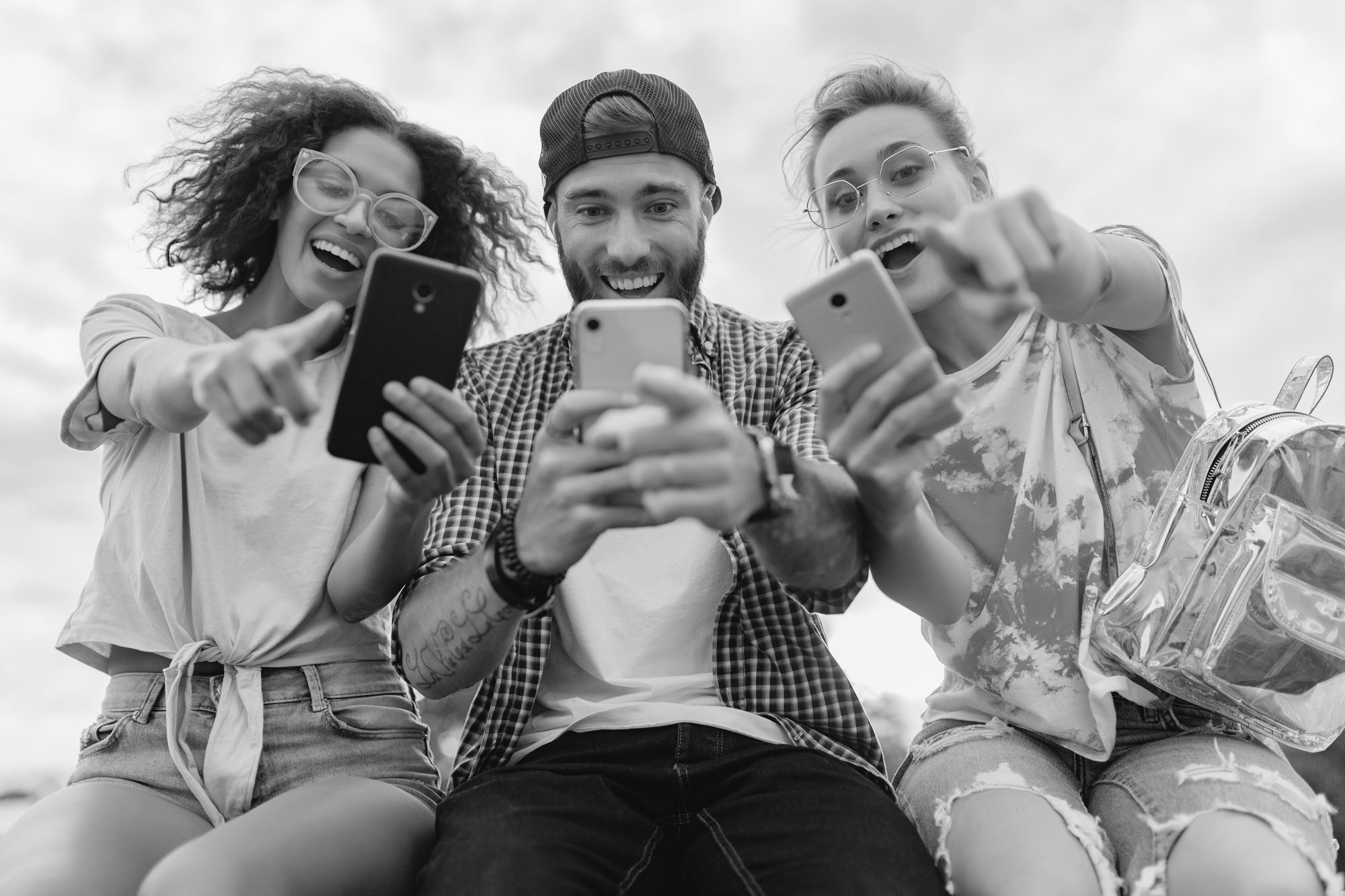 happy-young-company-smiling-friends-sitting-park-using-smartphones