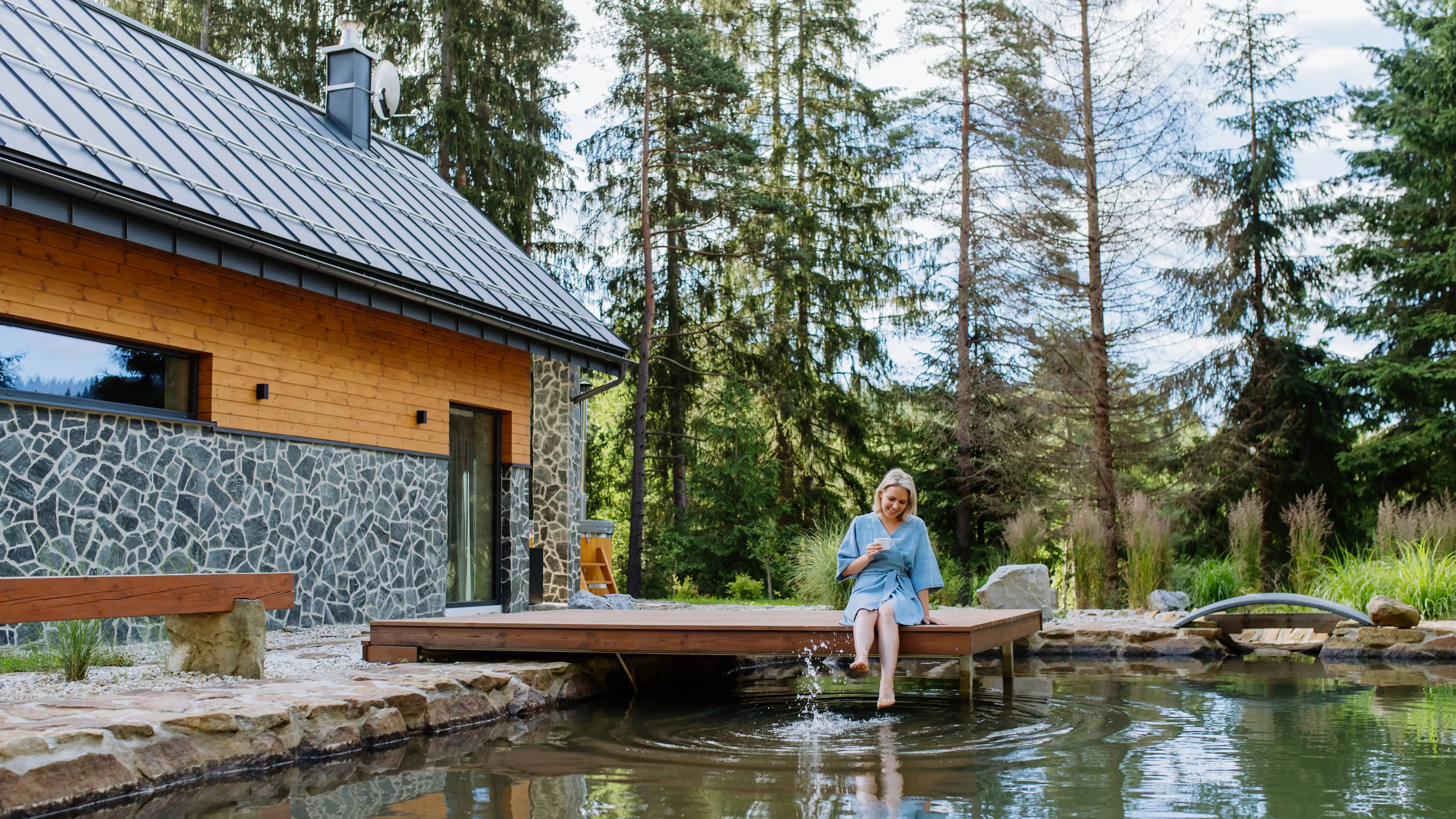 happy-young-woman-sitting-by-pond-near-cottege-and-2024-10-20-08-56-47-utc
