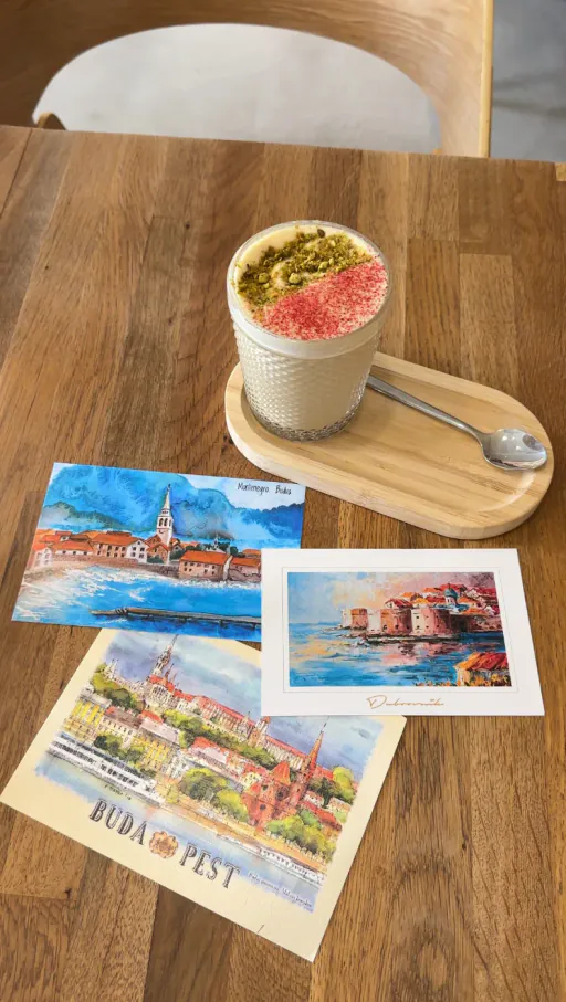 Dessert and Budapest, Dubrovnik and Budva postcards on a wooden café table